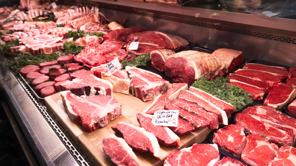 A fully stocked butcher display case showcasing a wide variety of fresh beef cuts including ribeyes, T-bones, and roasts.