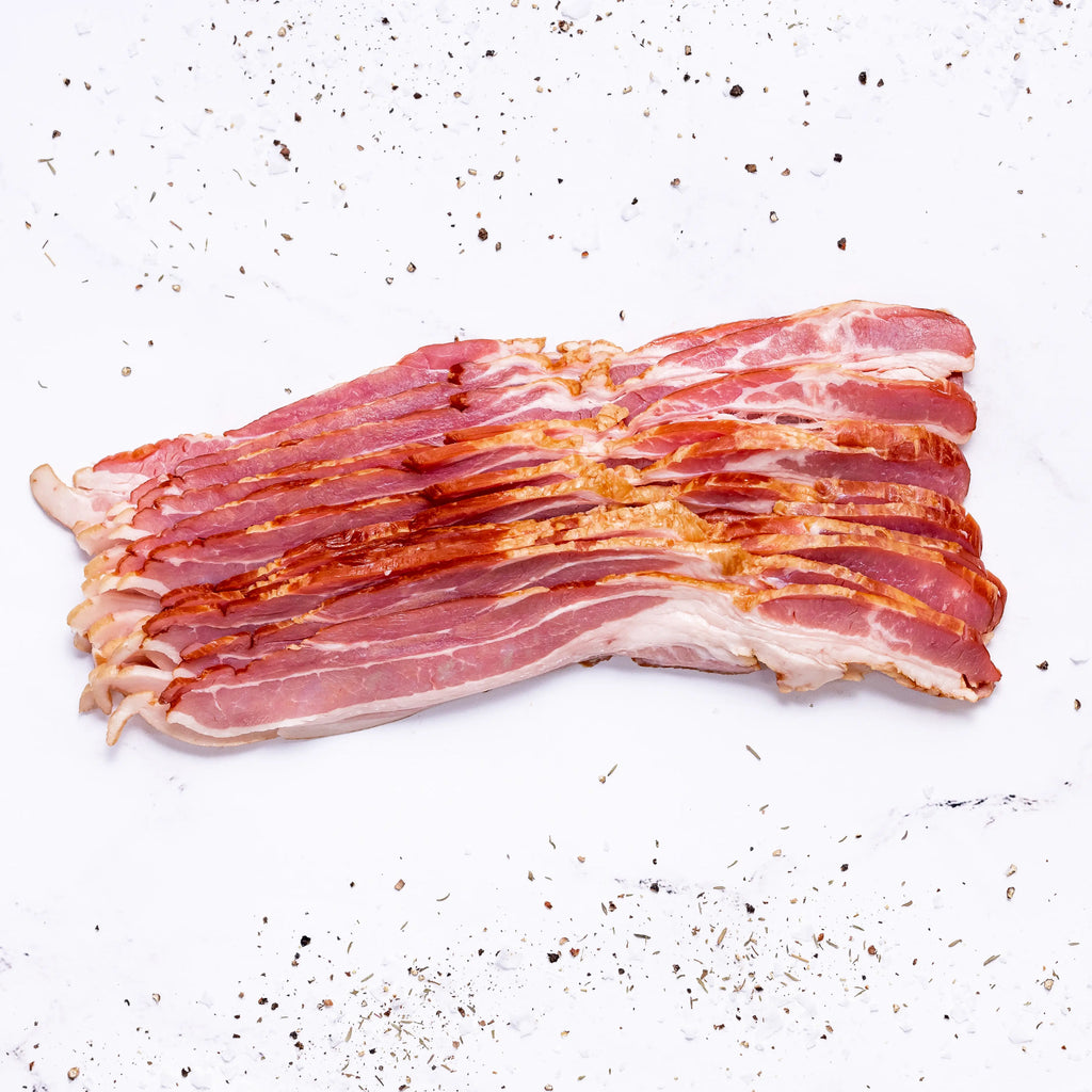 Several strips of FREE Applewood Smoked Uncured Bacon are layered on a white surface, with black pepper and seasonings scattered around.