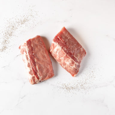 Two Pork Ribs, each about 1 lb, are displayed side by side on a white marble surface with black pepper sprinkled nearby—highlighting the contents of the Pork Ribs package.
