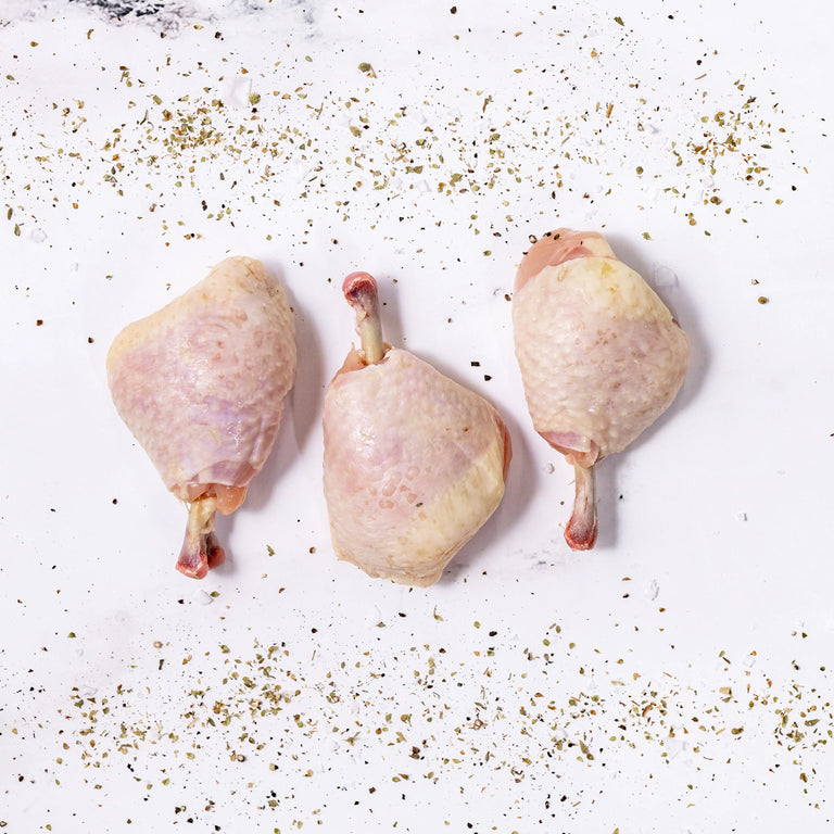 Three Chicken Lollipops with skin are arranged in a row on a white surface, surrounded by sprinkled dried herbs and spices.