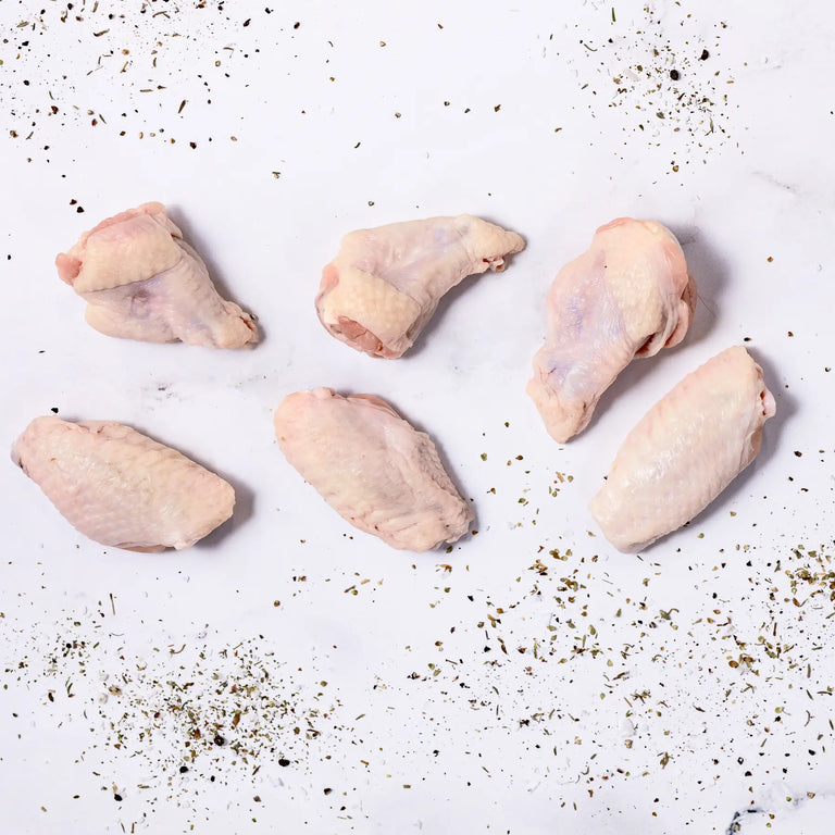 Six pieces of Chicken Wings are arranged on a white surface, with dried herbs and spices scattered around them.