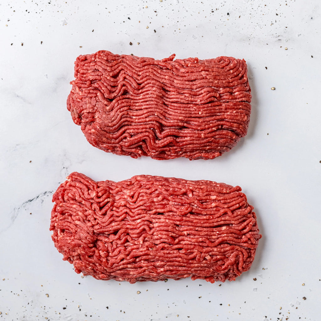 Two rectangular portions of FREE Angus Ground Beef on a white marble surface, sprinkled with black pepper.