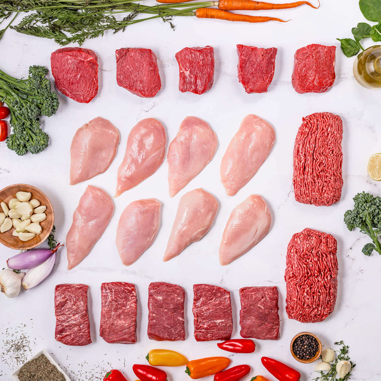 The Home Cook Box by Good Ranchers includes locally sourced chicken breasts, ground beef, stop sirloin steaks, flat iron steaks, and more. Here's a layout of the box contents, surrounded by fresh veggies, lemon, shallot, garlic, olive oil, and herbs.