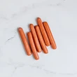 Six FREE Hot Dogs are arranged in a slightly fanned-out row on a white marble surface.