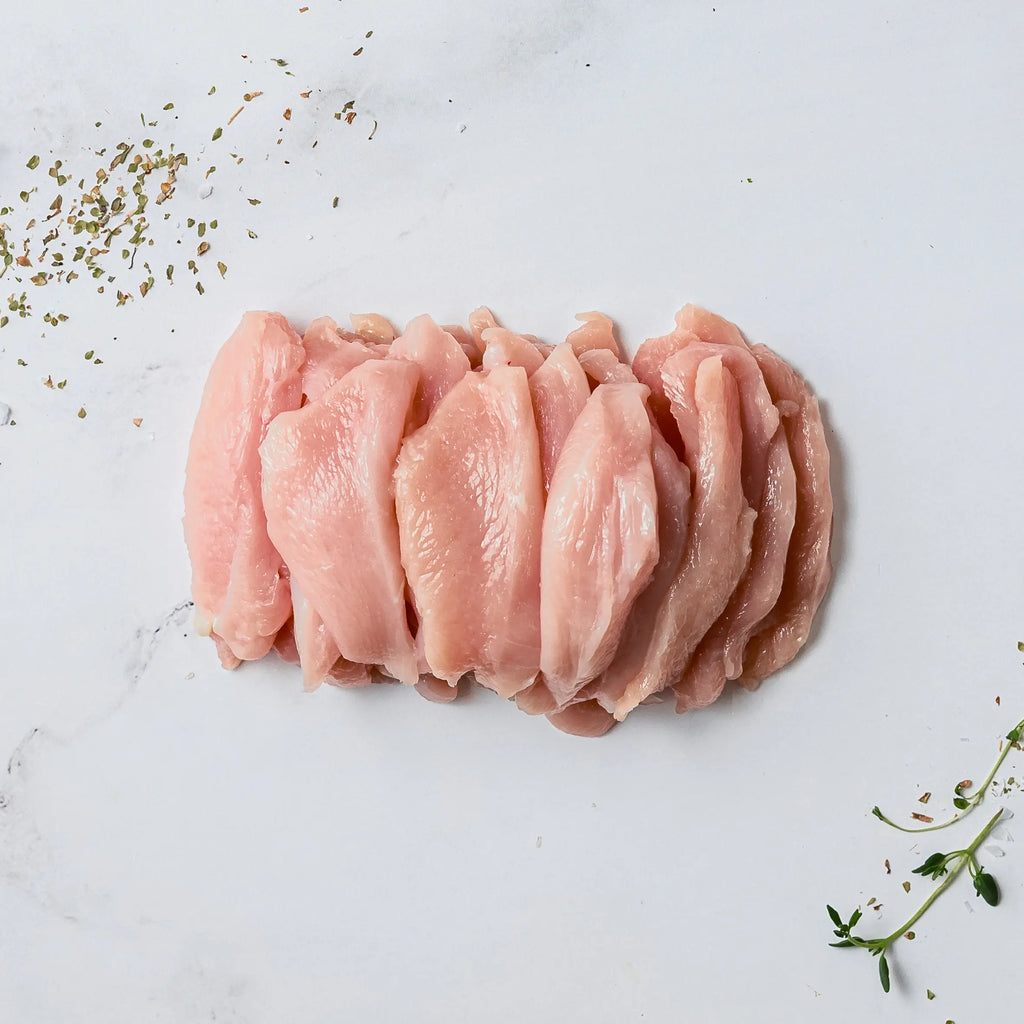 Strip Cut Chicken is displayed as raw, thin slices on a white marble surface, accompanied by scattered dried herbs and a fresh sprig of thyme.