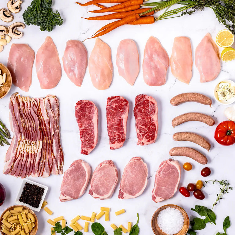 Ranchers Favorites features an assortment of locally sourced meats—from free Range chicken breasts, to pork chops, bacon, steaks, and sausages—neatly arranged on a white surface with vegetables, pasta, and seasonings.
