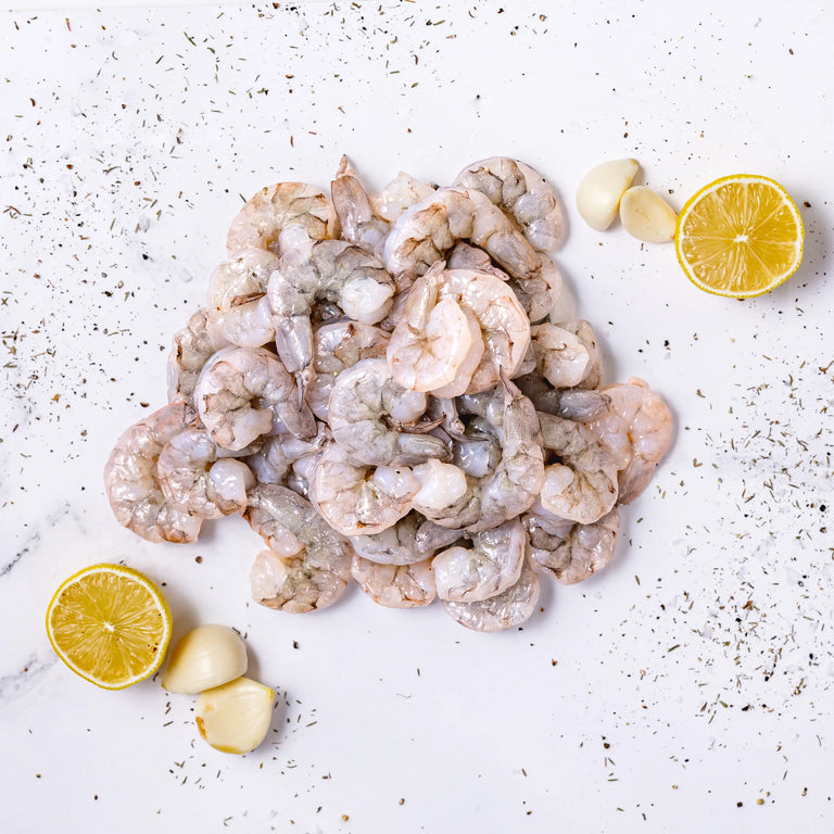 Wild-Caught Shrimp arranged on a white surface, accented with garlic cloves, two lemon halves, and a sprinkle of dried herbs.
