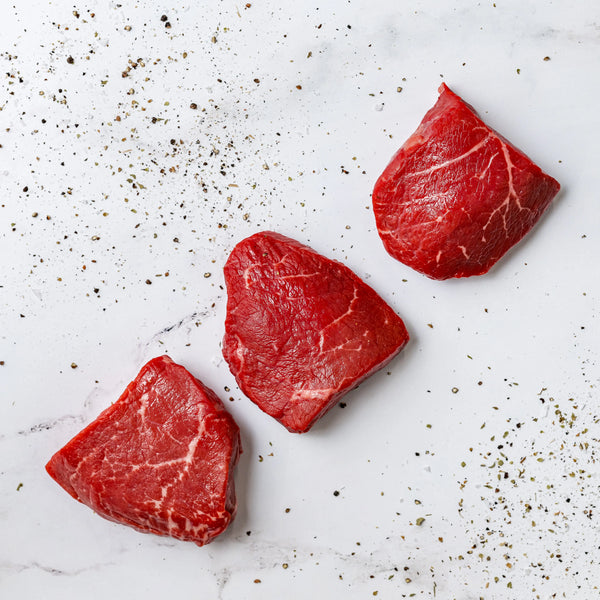 Three Top Sirloins are arranged on a white marble surface, sprinkled with coarse pepper and seasoning.