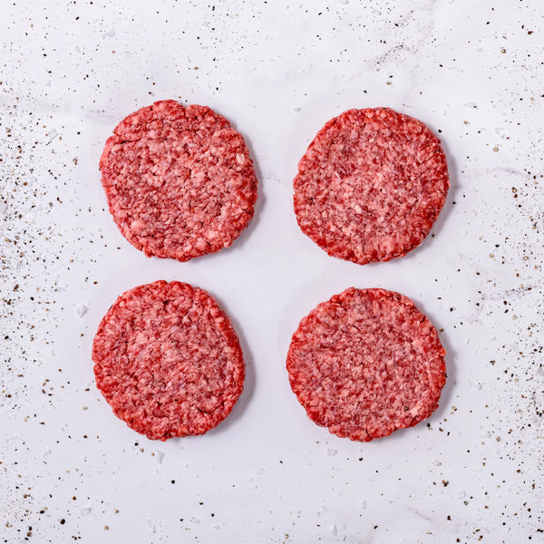 Four FREE American Wagyu + Angus burger patties arranged in a square on a white surface, with pepper and seasoning sprinkled around them.